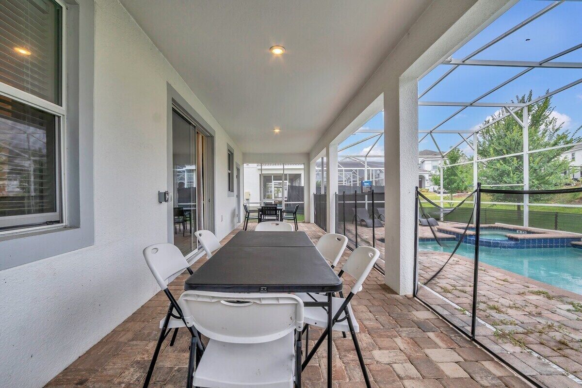 Un patio cubierto con mesa y sillas, una piscina y vistas del vecindario.
