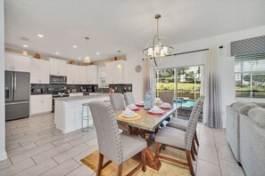 A modern kitchen with white cabinetry, a central island, and a dining area with grey upholstered chairs.