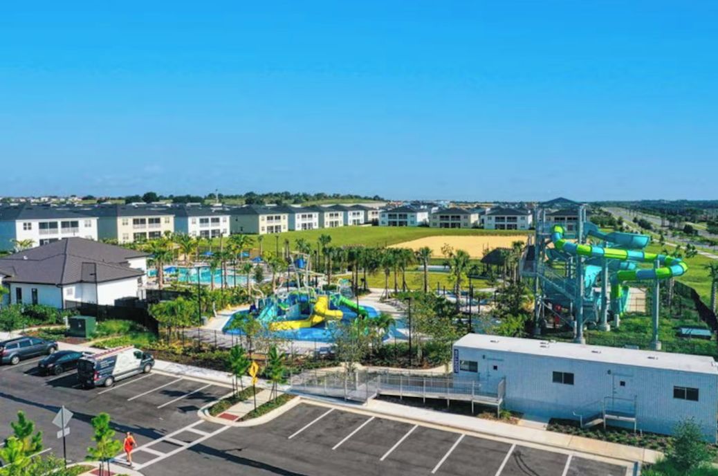 Um parque aquático com vários toboáguas e piscinas, cercado por edifícios e um estacionamento.