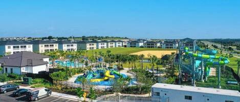 Um parque aquático com vários toboáguas e piscinas, cercado por edifícios e um estacionamento.