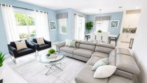 Una sala de estar moderna con un sofá modular, una mesa de centro de vidrio y un comedor con mesa y sillas blancas.