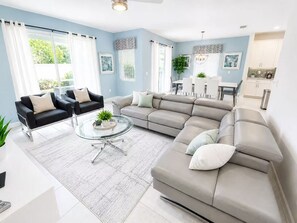 A modern living room with a sectional sofa, a glass coffee table, and a dining area with a white table and chairs. - Dazzling 6Br Villa W Pool&Spa(1564FD) (Davenport)