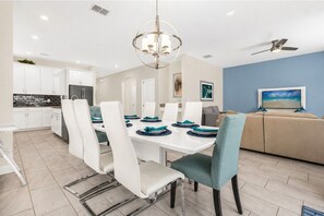 A modern dining room with a white table, teal chairs, and a chandelier.
