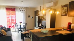 Una cuina moderna amb una illa central, zona d'esmorzar amb caires i taula, i un saló amb sofà.