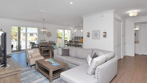 A spacious living room with a large sofa, a coffee table, and a TV. There is a dining area with a table and chairs, and a kitchen in the background. - Sombrero Beach Retreat w/ 60' Dock & Private Pool! (Marathon)