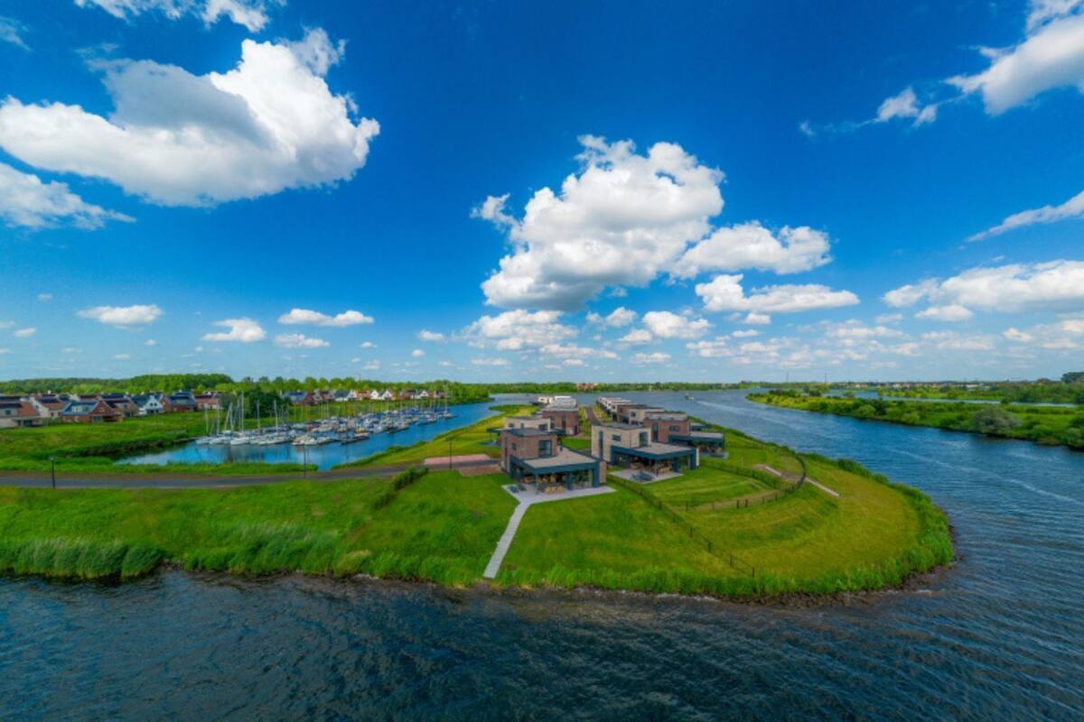 Une propriété située au bord de la rivière, avec des bâtiments modernes, un port de plaisance rempli de bateaux et une végétation luxuriante.