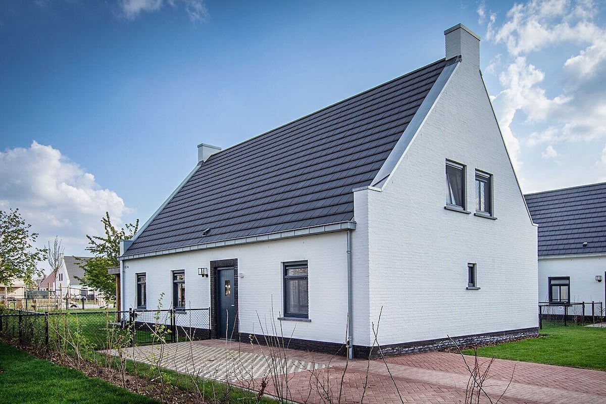 Un bâtiment blanc avec un toit foncé, un petit porche et un chemin en briques menant à l’entrée.