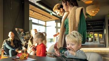 Una familia en un ambiente interior moderno con ventanas amplias, una mesa con una revista y una persona de pie con un niño.