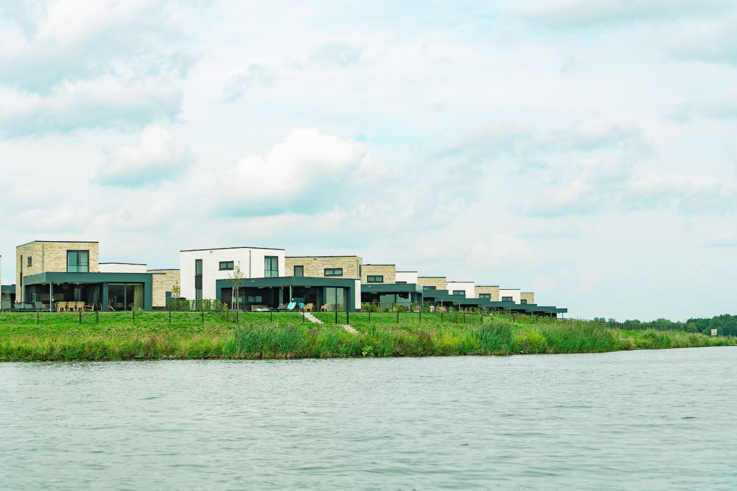 Un moderno complejo residencial a orillas de un río, con varias casas conectadas, grandes ventanales y techos planos.