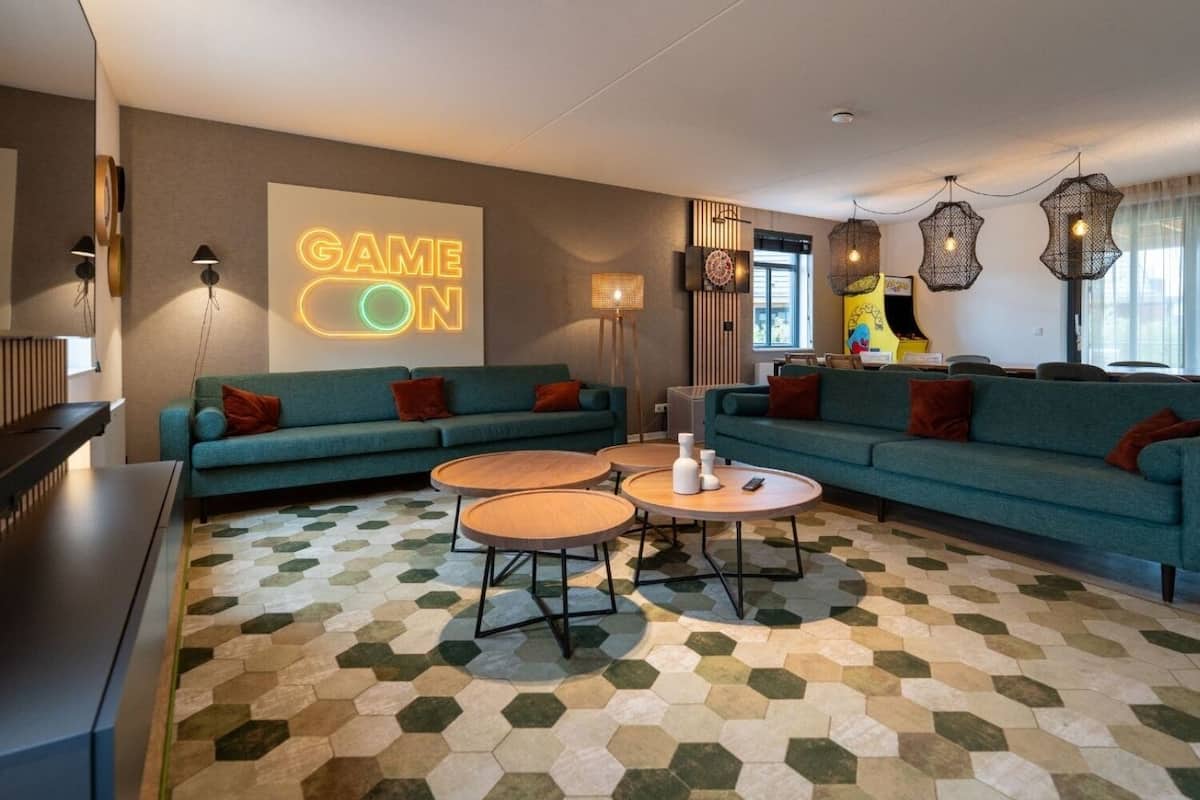 Un salon moderne avec des canapés de couleur turquoise, des tables basses en bois et un sol orné d’un motif hexagonal.