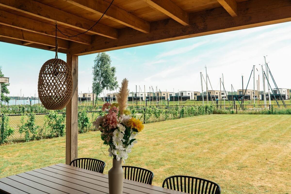 Une terrasse extérieure avec une table et des chaises en bois, une jardinière suspendue et une vue sur une marina remplie de bateaux.