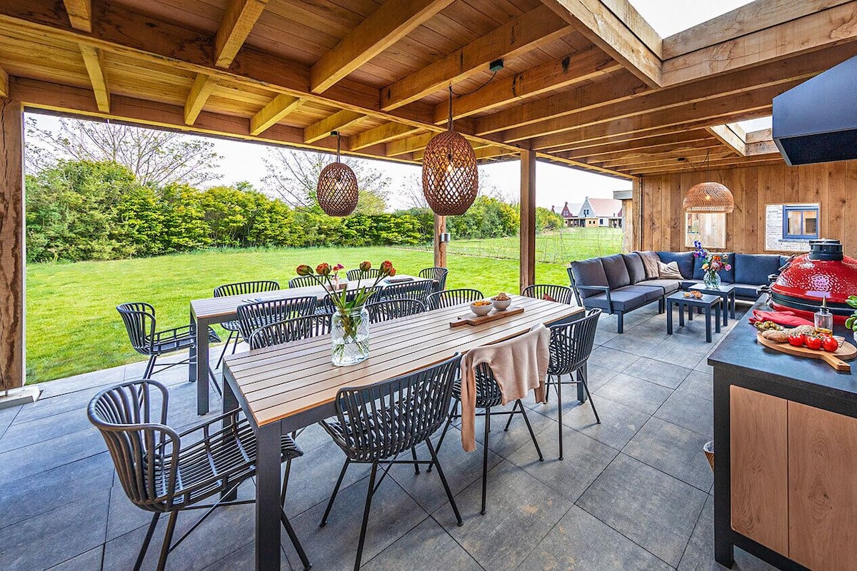 Une terrasse extérieure avec une table et des chaises en bois, un mur en briques et un espace barbecue.