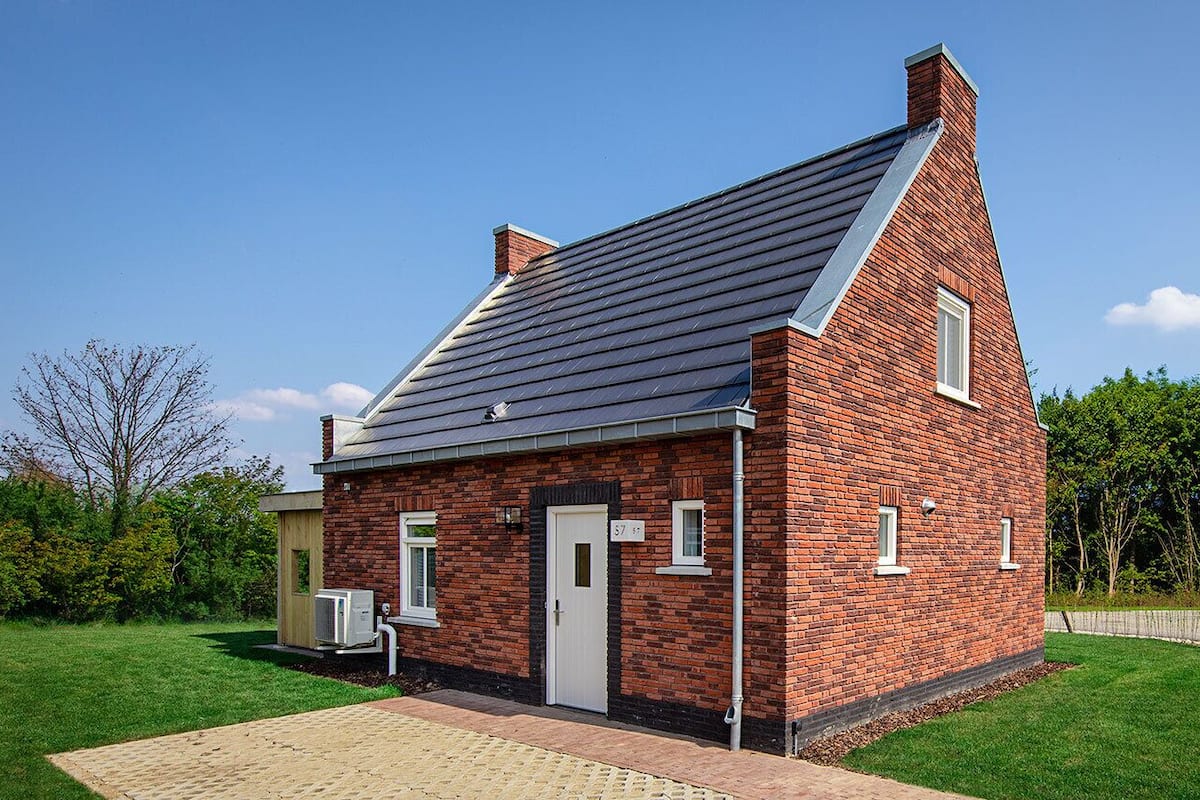 Une maison de plain-pied en briques, avec un toit en pente, une porte d’entrée et un petit garage attenant.