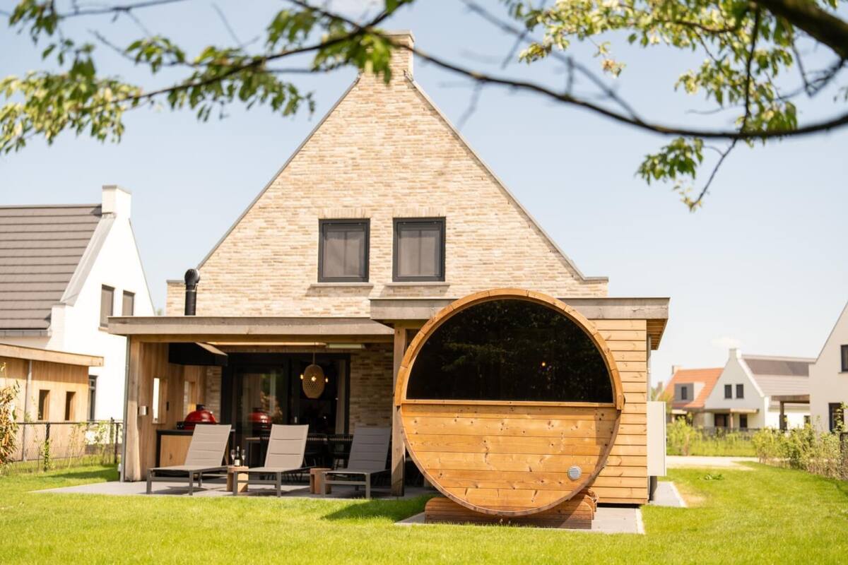 Une maison dotée d’une grande fenêtre en forme de tonneau en bois, d’un espace extérieur aménagé et couvert, et d’une pelouse bien entretenue.