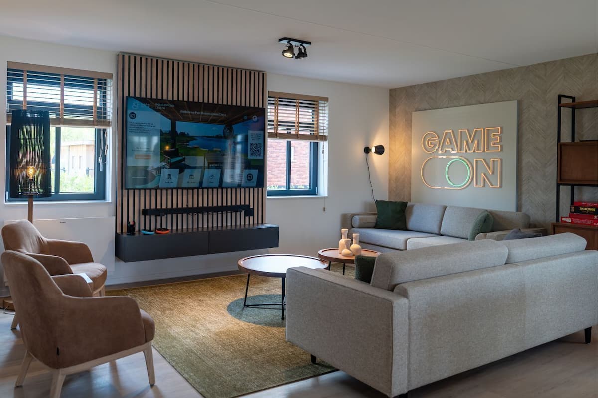 Un salon moderne avec un canapé gris, une table basse et un téléviseur fixé au mur, sur lequel on trouve un panneau en bois vertical.