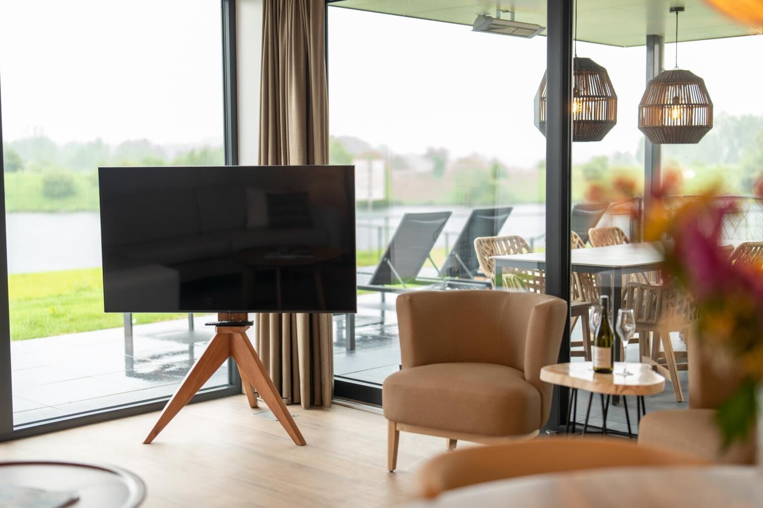 Ein modernes Wohnzimmer mit einem großen Flachbildfernseher auf einem Holzständer, einer gemütlichen Couch und einem Essbereich mit Korbstühlen und einem Tisch.