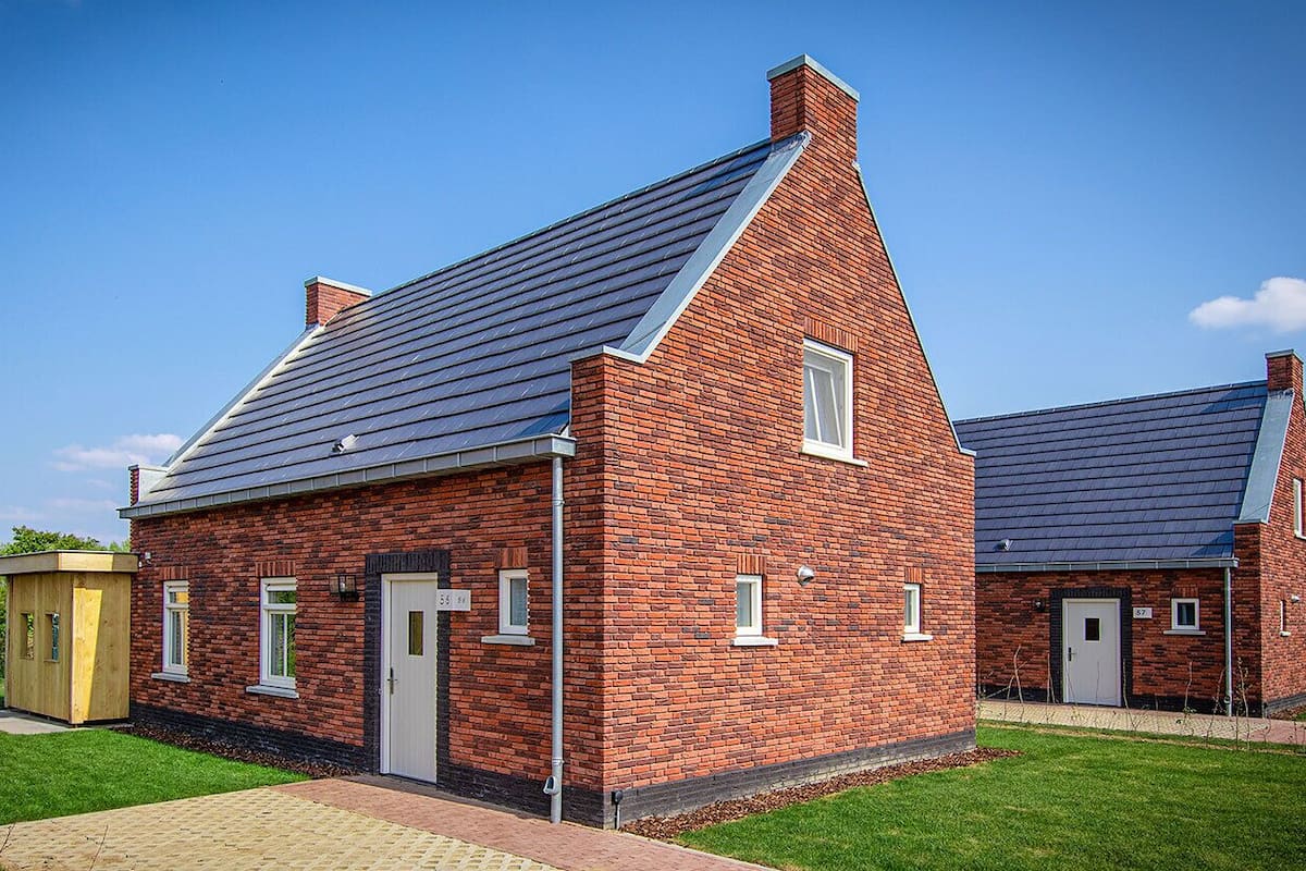 Un bâtiment en briques avec un toit en pente, une petite construction en bois sur la gauche et un ciel bleu dégagé.