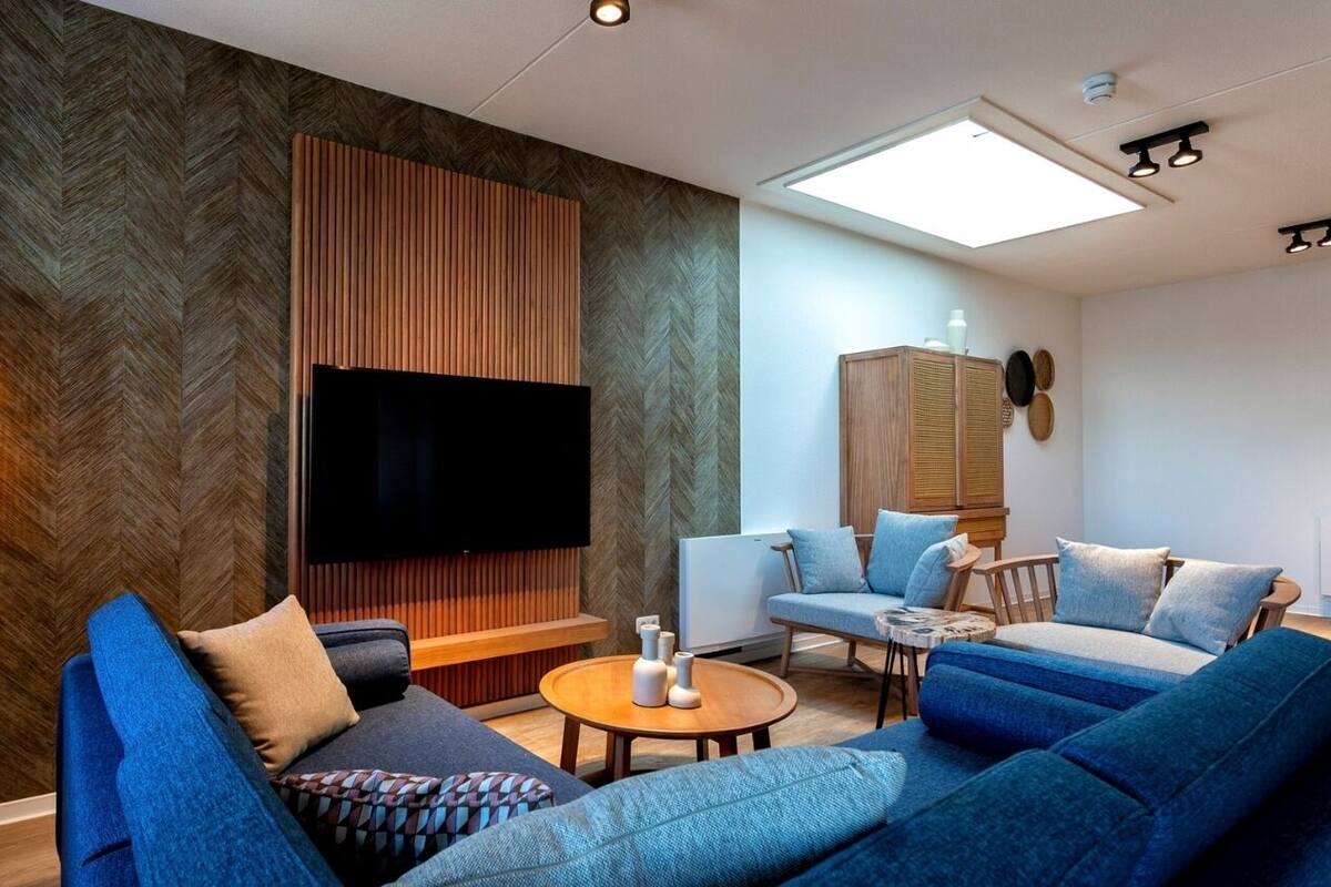 Un salon moderne doté d’un grand téléviseur à écran plat, de canapés bleus, d’un mur d’accent en bois et d’un luminaire au plafond.