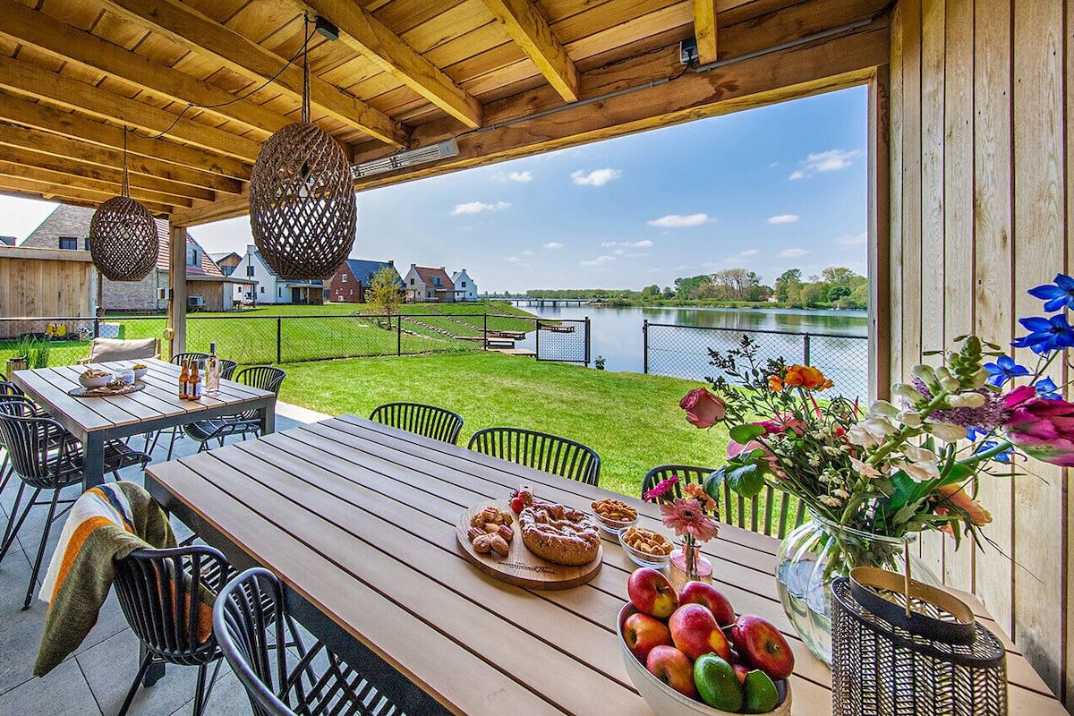 Une terrasse extérieure avec une table en bois, des chaises et une vue sur un lac.