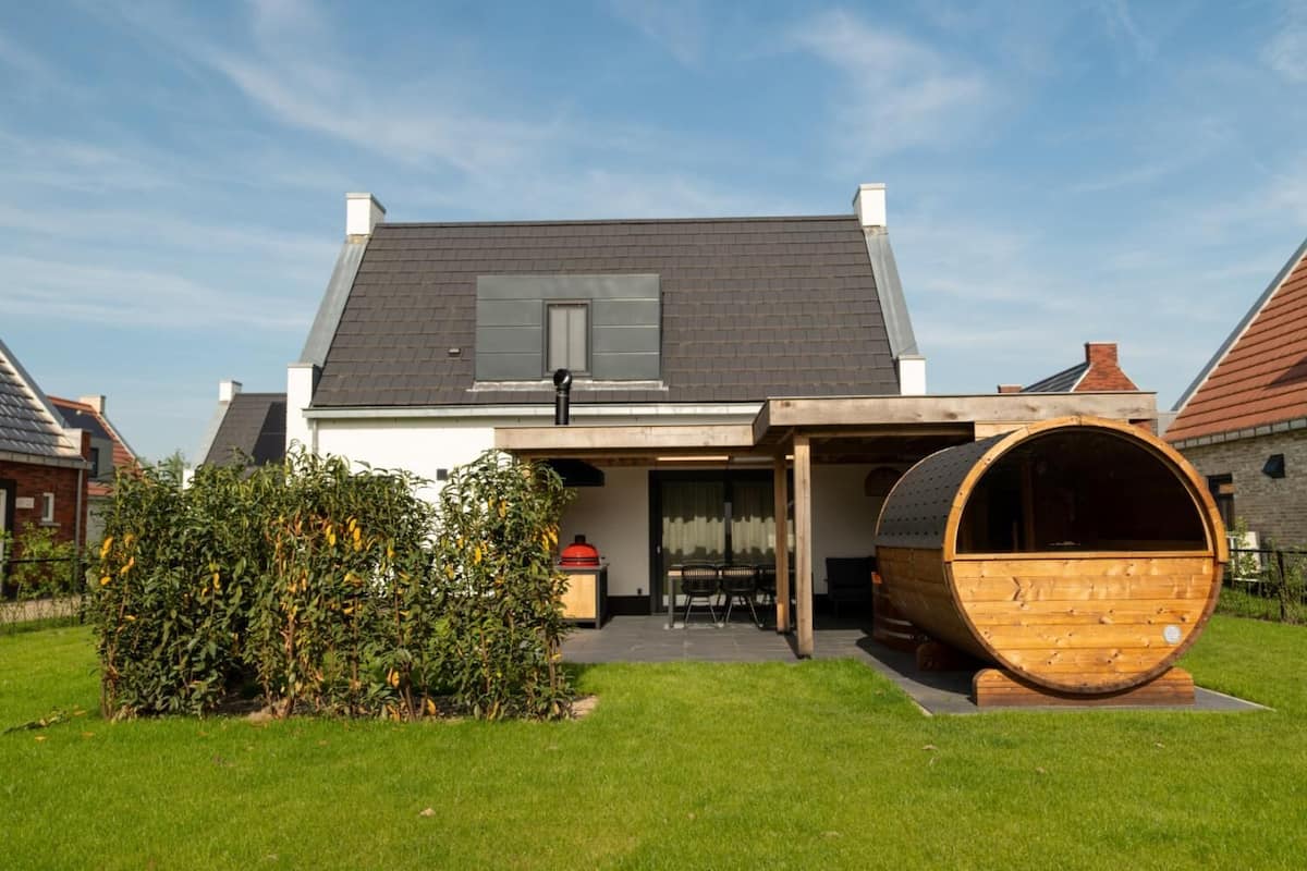 Une maison moderne avec une grande structure en forme de tonneau située dans le jardin avant.