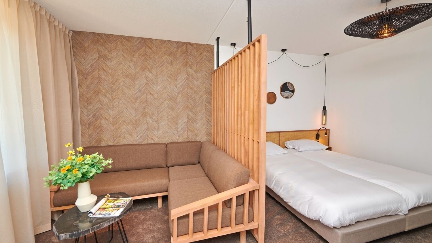 Ein gemütliches Hotelzimmer mit einer Couch, einem Einzelbett, einem kleinen Tisch mit Blumenvase und einer Wandleuchte.