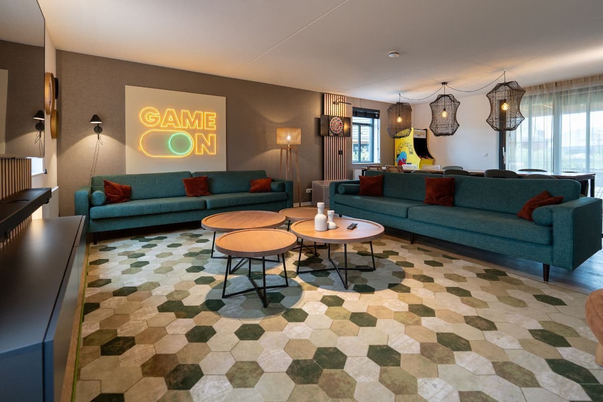 Un salon moderne avec des canapés de couleur turquoise, un néon affichant le message « GAME ON » et un sol à motifs géométriques.