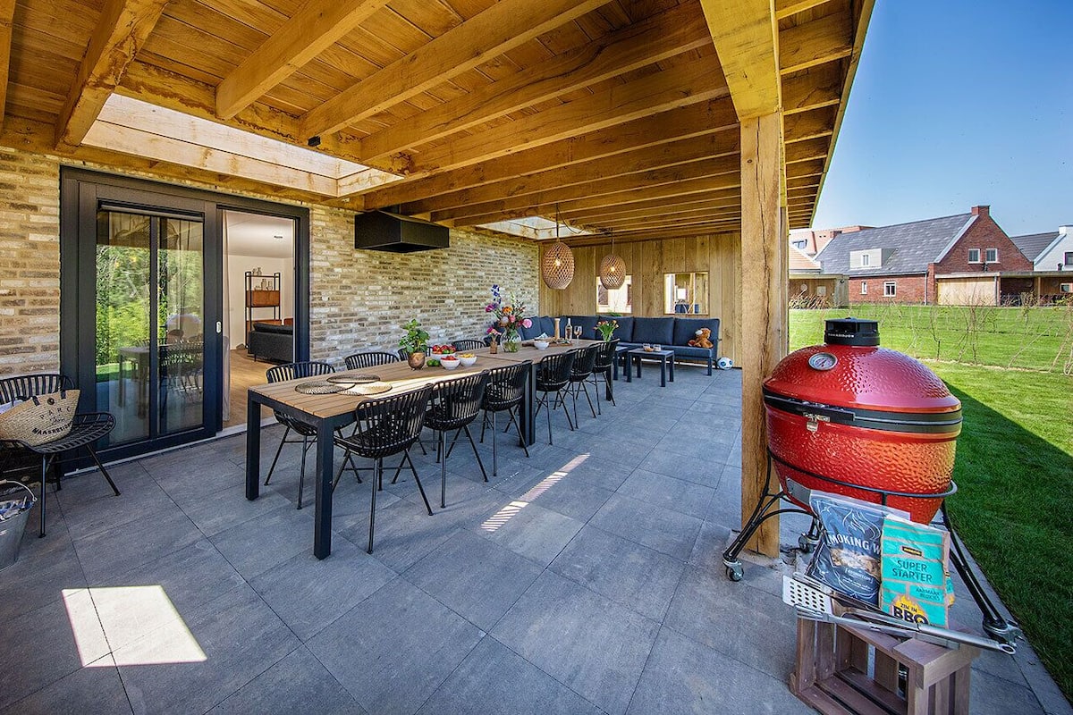 Une terrasse extérieure avec une table et des chaises en bois, un barbecue et un mur en pierre.