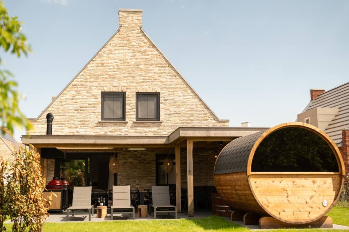 Une maison avec une façade en pierre, un toit à deux versants et un grand tonneau en bois placé au premier plan.