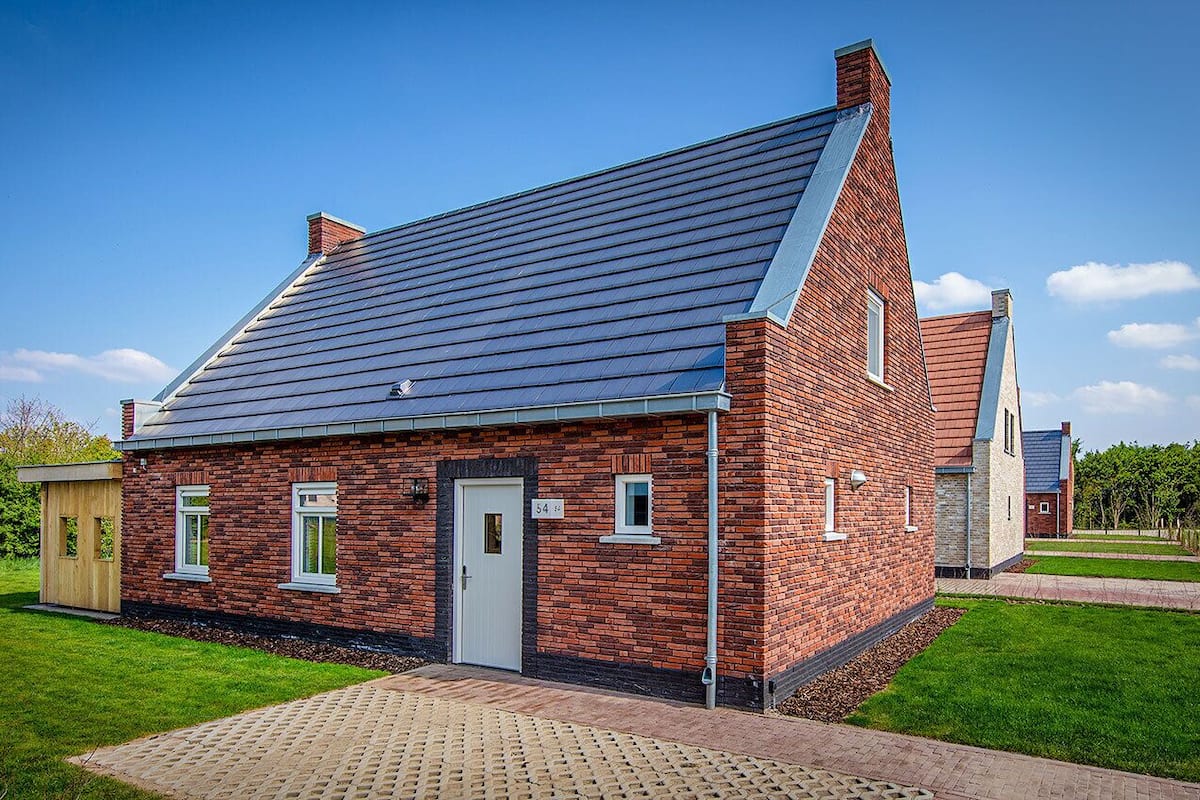 Une maison en briques rouges, avec un toit en pente, un petit porche et une allée pavée.