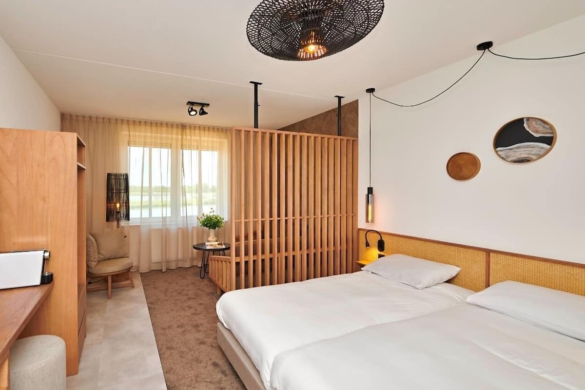 Une chambre d’hôtel moderne avec un grand lit, un bureau avec un ordinateur, une chaise et une petite table agrémentée d’une plante.