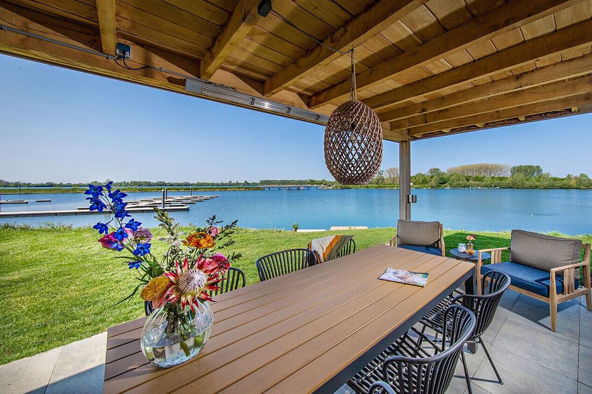 Un espace extérieur aménagé pour les repas, avec une table et des chaises en bois, un objet décoratif suspendu et une vue sur un lac.