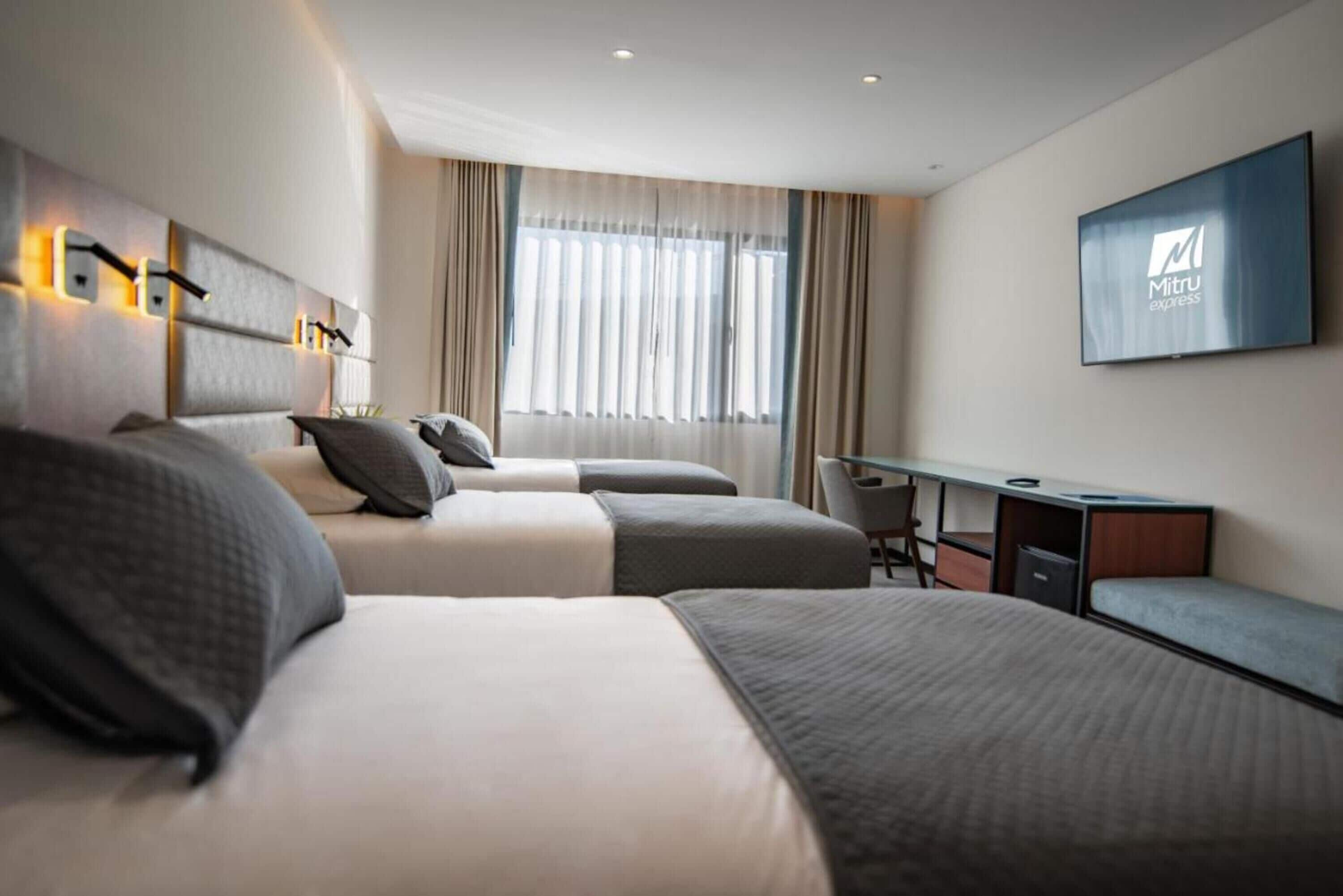 A modern hotel room with two beds, a desk, and a television.