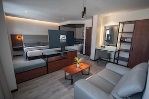 Habitación de hotel moderna con cama, sofá, televisión, escritorio y una planta pequeña.