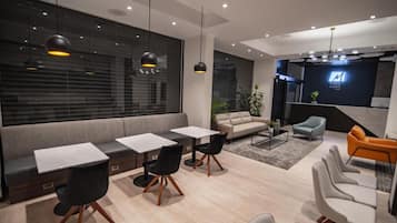 A modern interior with a sofa, two tables with chairs, a coffee table, and a TV mounted on the wall.