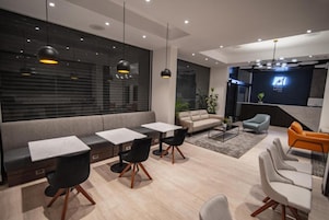 Un interior moderno con un sofá, dos mesas con sillas, una mesita de centro y un televisor montado en la pared.