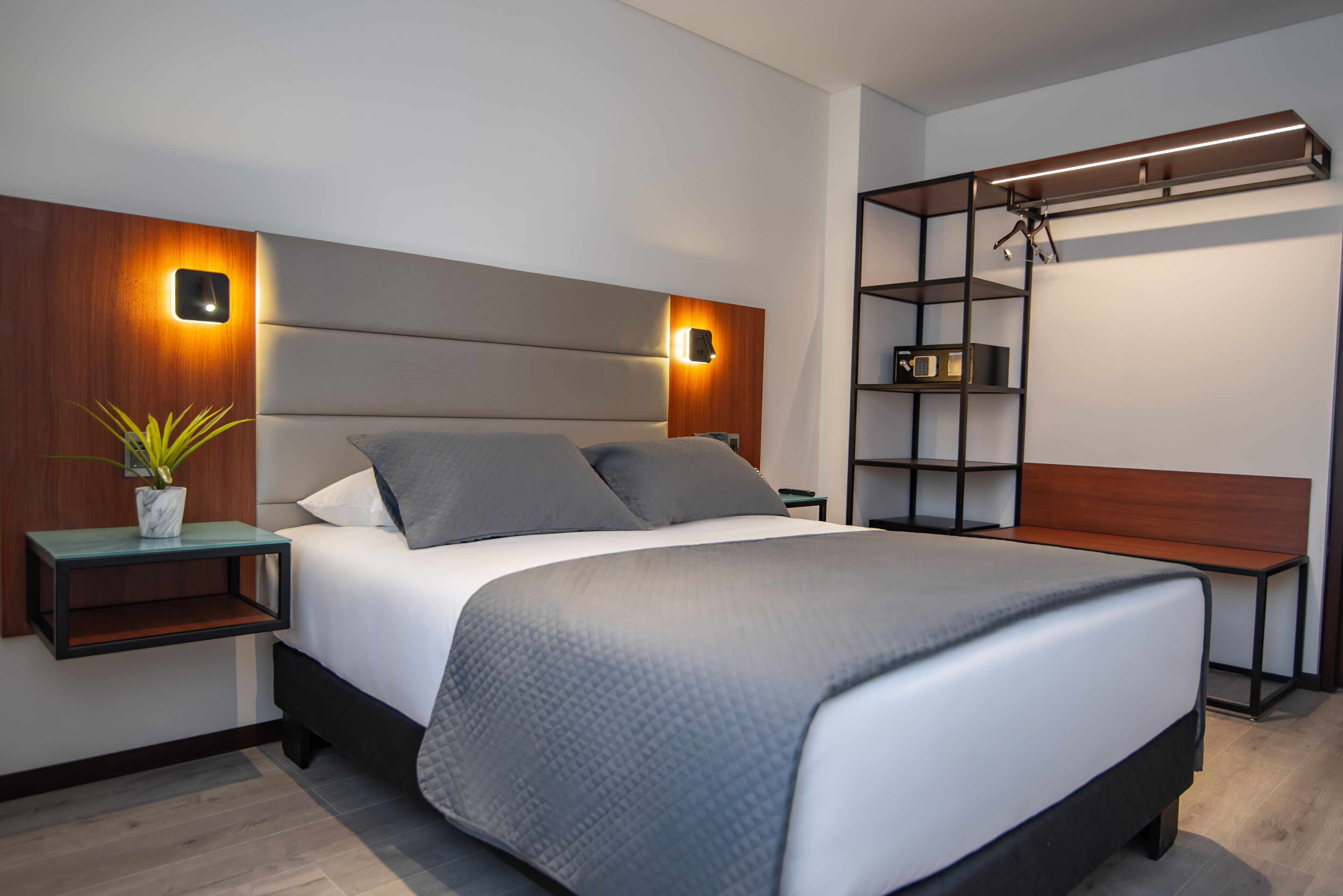 A modern bedroom with a large bed, bedside tables, a nightstand, a wall-mounted shelf, and a hanging light fixture.