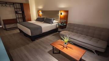 A modern hotel room with a bed, a sofa, a nightstand, a lamp, and a small table with a plant.