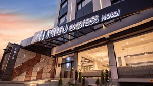 Una entrada de hotel moderna con fachada geométrica, un número de dirección visible y una zona de recepción bien iluminada.
