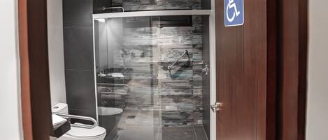 A modern bathroom with a glass shower enclosure, a white toilet, and a disabled access sign.