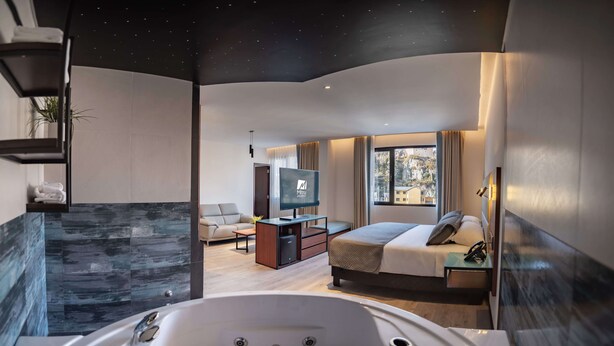 Habitación de hotel moderna con una bañera grande, un sofá, un televisor y vistas al exterior.