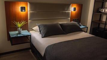 A modern bedroom with a large bed, two bedside tables, a nightstand, a wall-mounted lamp, and a small potted plant.