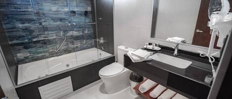 Un baño moderno con ducha de vidrio, inodoro blanco, lavabo con tocador y espejo con secador de pelo.