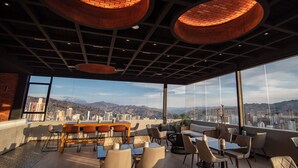 Un espacio moderno para comer en la azotea con vistas a la ciudad, amplias ventanas y mobiliario contemporáneo.