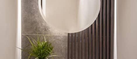 Un baño moderno con un espejo grande, una planta en maceta y un estante oscuro.