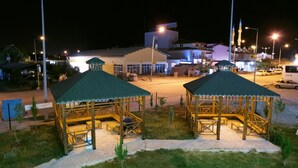 A gazebo with a tiled floor and a green roof, surrounded by grass and a paved walkway.