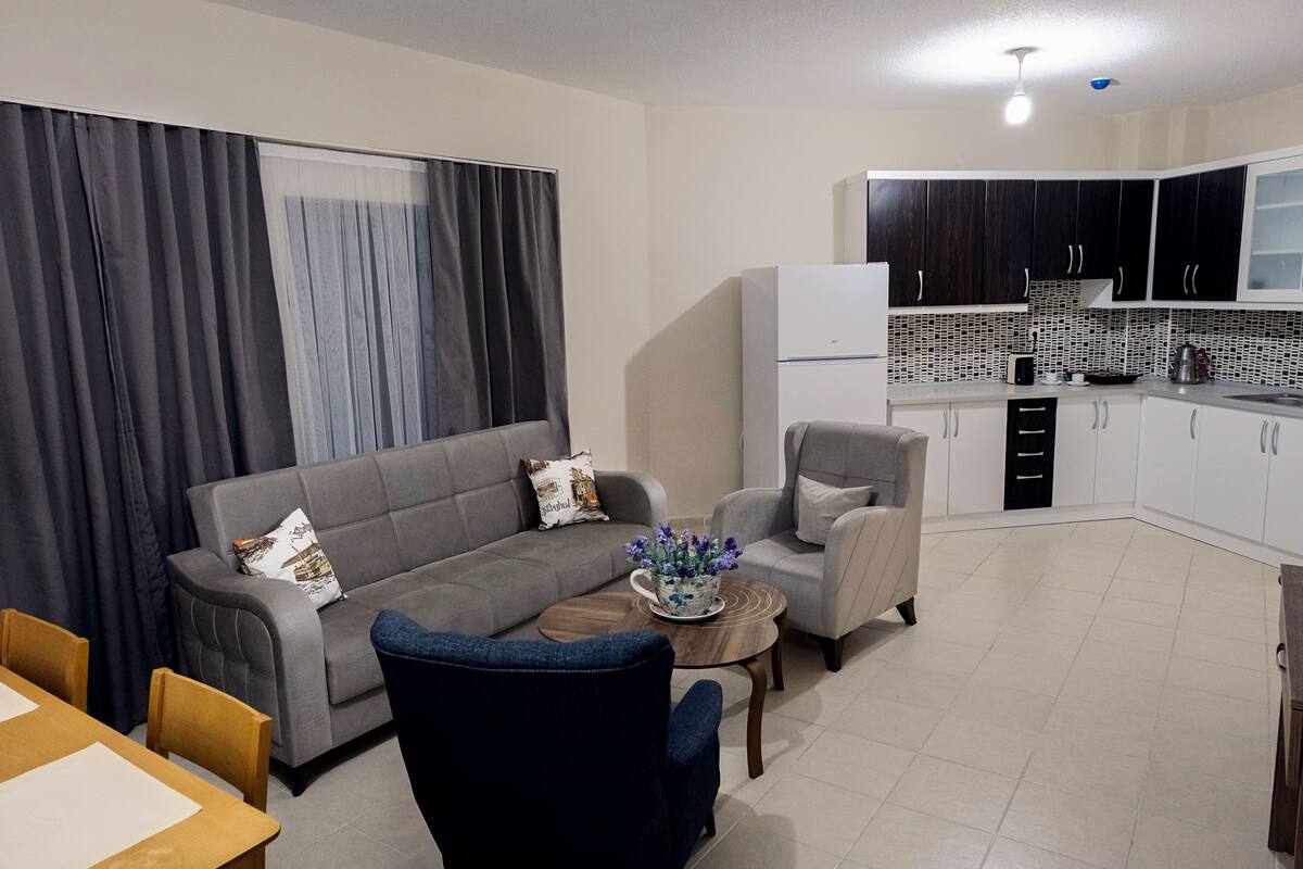 A modern living room with a grey sofa, a coffee table, and a dining area with a wooden table and chairs.