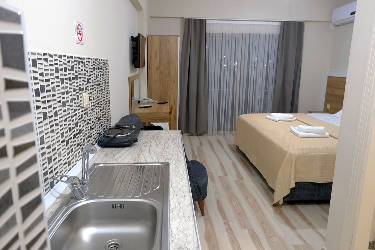 A hotel room with a marble countertop sink, a bed with a beige bedspread, a wooden wardrobe, and a television mounted on the wall.
