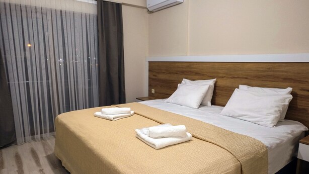 A hotel room with a bed, a wooden headboard, a nightstand, and a window with curtains.