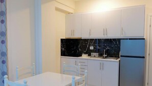 Una cocina compacta con armarios blancos, encimera de mármol negro y refrigerador de acero inoxidable.