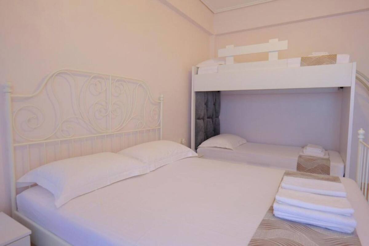 Una habitación de hotel con estructura de cama metálica blanca, dos camas y toallas dobladas cuidadosamente sobre la cama.